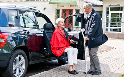 Man assisting woman our of a outward facing seat in a car